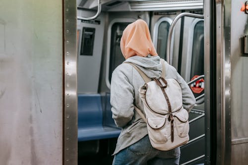 Free Muslim woman with a backpack and hijab enters a subway train, showcasing urban lifestyle. Stock Photo