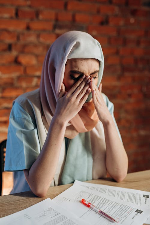 Free Middle Eastern woman in hijab looking stressed at work desk. Stock Photo